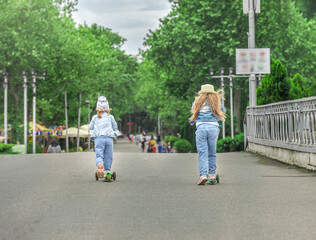 Two sisters on scooters take a walk in a public park, they are fun and active on the high road.