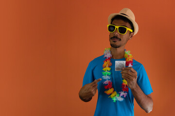 Black man in costume for brazil carnival holding  a condom isolated on orange background. African...