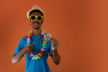 Black man in costume for brazil carnival holding  a condom isolated on orange background. African...
