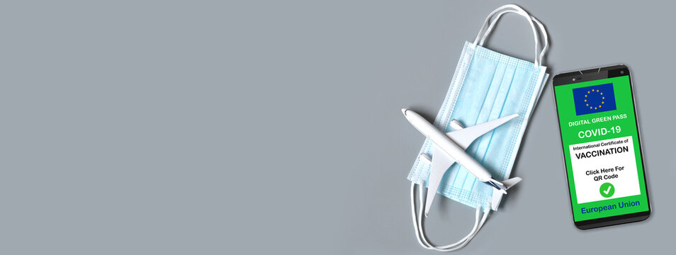 Traveling during the coronavirus pandemic. Smartphone with european digital covid-19 vaccination certificate along with protective masks and airplane model on grey background. Safe travel concept.