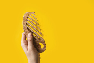 Women's hand hold a natural wooden comb with hair falling out of the head on yellow background. Cosmetic and medical hair care oils with vitamins and prebiotic serum.