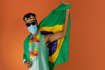 Black man in costume for carnival with brazil flag and pandemic mask isolated on orange background. African man in various poses and expressions.