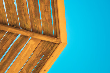 Detail of bright yellow wood beach umbrella under clear sky. Wooden structure. Colorful travel composition. Symbol of summer vacation