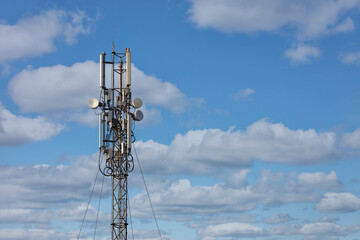 Cellular antennas on a metal mast against a blue cloudy sky.