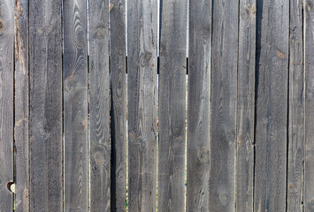 Texture of an old wooden fence with weathered boards in the sunlight.