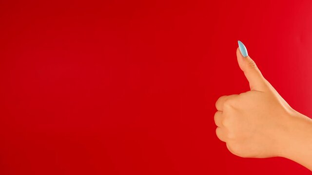 Woman's hand showing thumb up on red background with space for text. Unrecognizable person showing gesture of like.