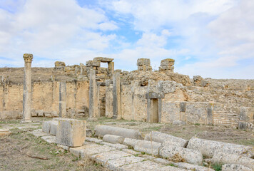 Obraz premium Ruins of the antique Roman city of Thugga in Tunisia, Africa. Yellow and grey stone standing and lying ruined columns, blue sky with clouds