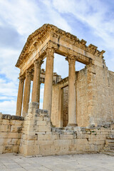 Obraz premium Temple of Jupiter, forum and ancient roman ruins of Dougga in Tunisia, Africa in the sunny afternoon. Blue sky with clouds, old yellow, grey and brown stone walls and columns 