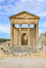 Temple of Jupiter, forum  and ancient roman ruins of Dougga in Tunisia, Africa in the sunny afternoon. Blue sky with clouds, old yellow, grey and brown stone walls and columns 
