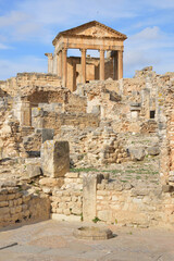 Fototapeta premium Temple of Jupiter and ancient roman ruins of Dougga in Tunisia, Africa in the sunny afternoon. Blue sky with clouds, old yellow, grey and brown stone walls and columns 