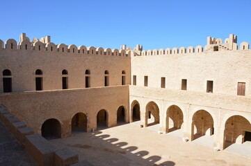 Fototapeta premium The inner yard of VIII century arabic fortress (ribat) in Sousse, Tunisia, Africa. Blue sky, old arches, shadows and sunlight on the ancient stone walls