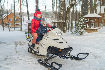 Fototapeta na wymiar mom and son sit on a snowmobile in the snow-covered forest winter fun