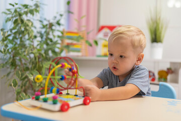 little boy child blonde play with toy to sit at the table at home.