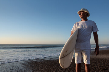Senior adult man at the beach with his surfboard