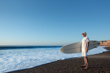 Senior adult man at the beach with his surfboard