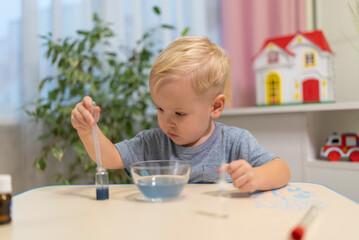 little boy child blonde play chemical experiments to sit at the table at home.