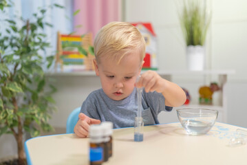 little boy child blonde play chemical experiments to sit at the table at home.