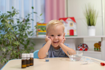 little boy child blonde play chemical experiments to sit at the table at home.