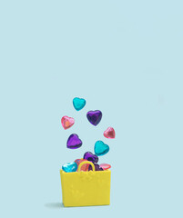 XOXO minimal modern concept. Yellow shopping bag full of different color crystal hearts rise and hover out of it. Baby blue background