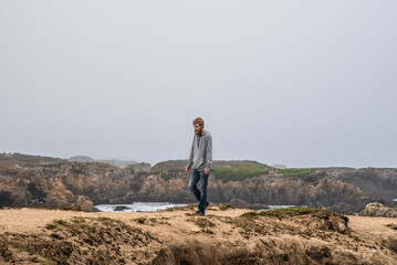 Obraz premium Man Hiking Through Tide Pools Along California Coast on a Cloudy Day at Fort Braggs