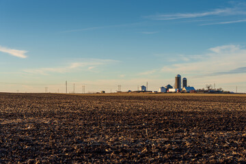 A winter farm field with distant silos and farm buildings
