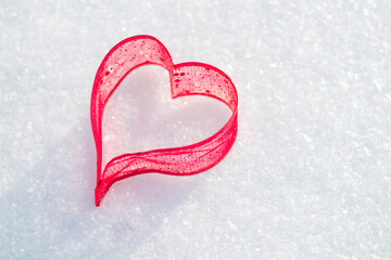 A red heart lies in the snow on a sunny day,