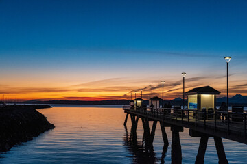 Fototapeta na wymiar Sun sets over Puget Sound and the Olympic Mountains with colorful skies and a fishing pier