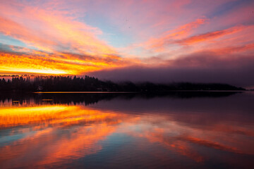 Sunrise over Lake Washington results in a colorful sky and reflection on the water, with foggy forest in the foreground