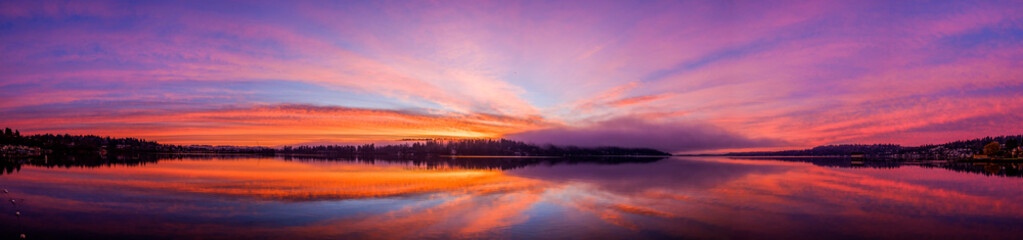 Fototapeta na wymiar Sunrise over Lake Washington results in a colorful sky and reflection on the water, with foggy forest in the foreground
