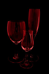 Three empty wine glasses with black background and red tint.