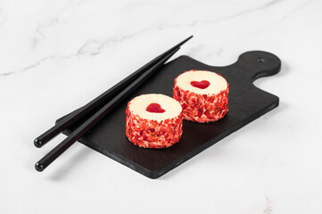 Sweet festive round sushi with jelly in the shape of a heart, sprinkled with small pieces of freeze-dried strawberries on a serving board on a white background. Valentine's Day