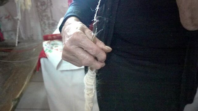Mature woman spinning white wool on spool