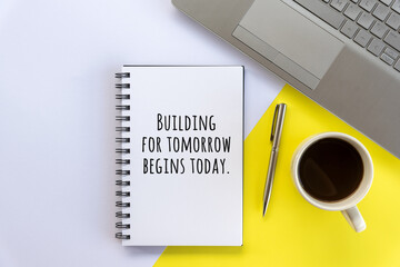Business motivational words on a book - Building for tomorrow begins today. A flat lay concept with cup of coffee, a book, pen and laptop on white and yellow table background.