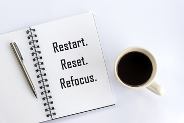 Restart. Reset. Refocus. Positive motivational words on book page with silver pen and a cup of morning coffee on white table background. Business evaluation concept.  - obrazy, fototapety, plakaty