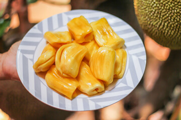 Jackfruit is fresh in a white plate, placed on a wooden table with jackfruit branches.