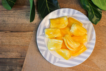 Jackfruit is fresh in a white plate, placed on a wooden table with jackfruit branches.