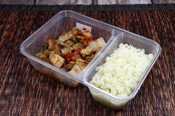 Famous spicy crispy pork serving with cauliflower rice in the plastic box. Mock up of ketogenic food concept. 