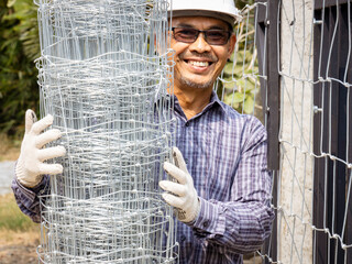 Close-up of half a technician installing a steel mesh fence on a very sunny day.