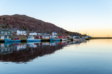 A view of Petty Harbour, Newfoundland, a small fishing village with a sheltered harbor surrounded by small fishing boats. The vintage houses surrounding the water are colorful wooden buildings. 