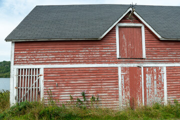 A vintage red two story barn with white trim, black shingled roof with multiple doors and windows....