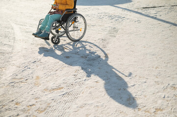 Close-up of hands of a disabled woman in a wheelchair outdoors in winter.
