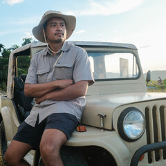Smart asian camping man sitting on vintage car outdoor recreation wear adventure hat