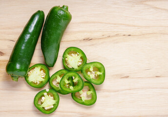 Whole fresh jalapeno peppers and slices on wooden board