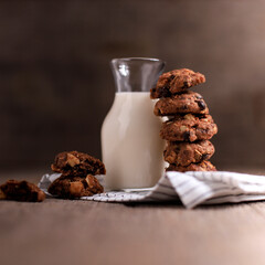 Stacked Homemade Chocolate Chips Cookies with Macadamia Nut, Served with a Bottle of Milk. Copy Space for Text, Recipe or Advertisement on Wooden Rustic Background. Selective Focus