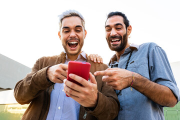 Young male gay couple look at mobile phone. Caucasian men watch funny videos on cellphone together.