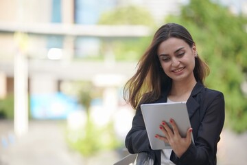 A businesswoman in professional attire uses a tablet while standing in an outdoor office environment, highlighting modern business practices and technology.