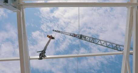 Bottom view of a tower crane. Construction crane on a background of blue sky with clouds. The hook of the construction crane hangs above the camera