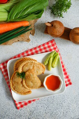 a plate of fried pastries containing vegetables served with sauce against white background