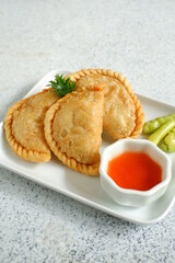 a plate of fried pastries containing vegetables served with sauce against white background