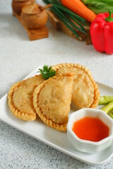 a plate of fried pastries containing vegetables served with sauce against white background